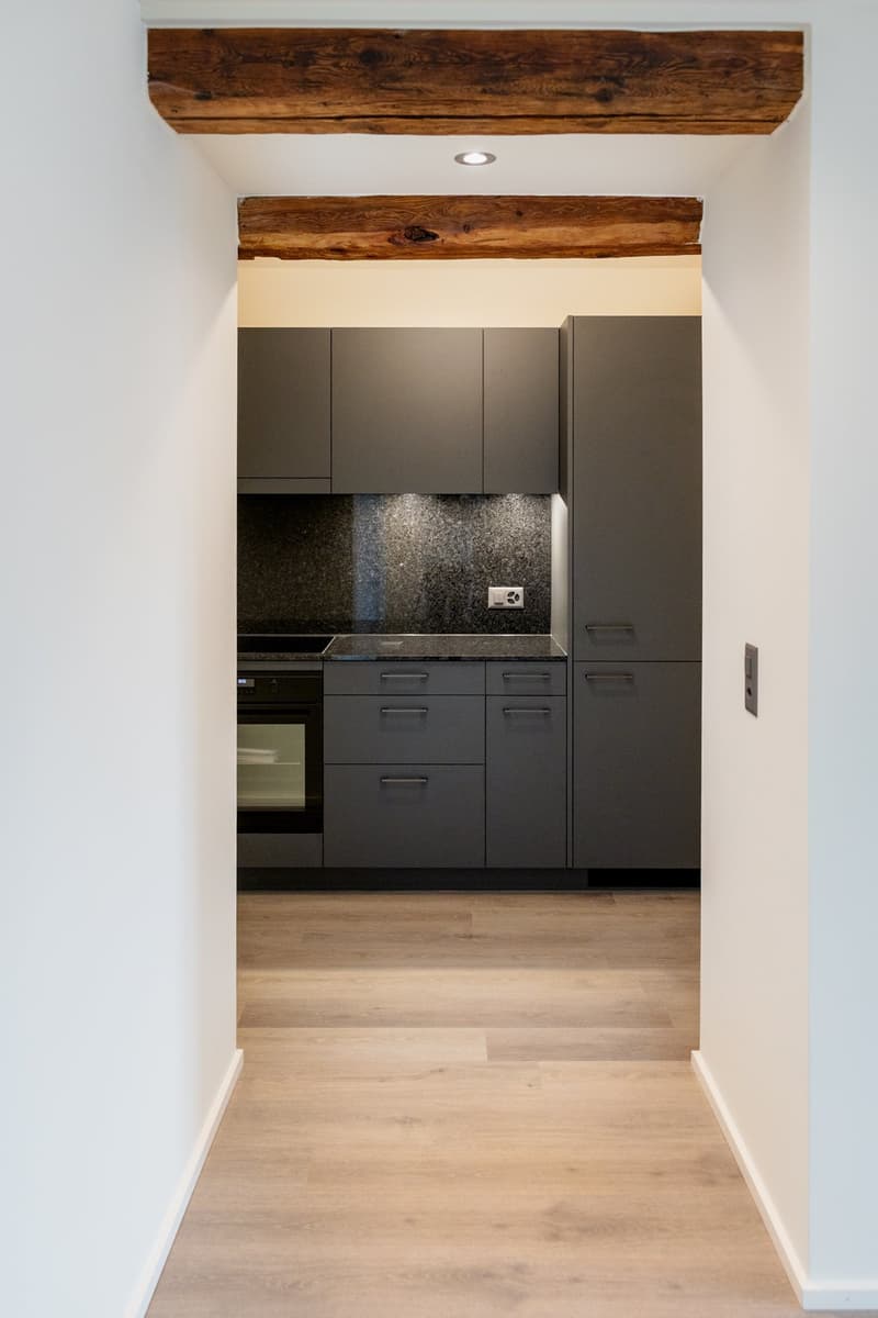 modern design, gray cabinets, wooden countertops, white tiled backsplash, dark gray oven, black granite tile, wood beams, white walls, wooden floor