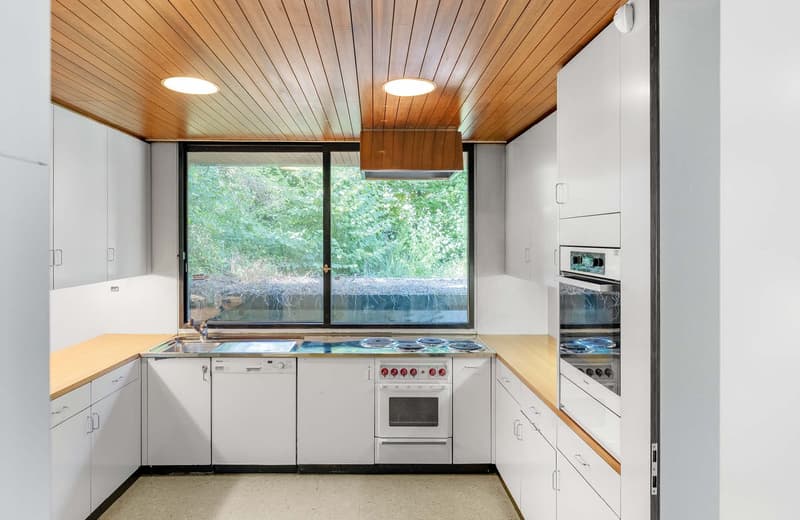 Contemporary kitchen with white cabinetry, wooden countertops, gas stove with oven, dishwasher, sink, and large window with outdoor view.