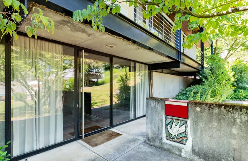 Modern architectural style, metal railings on balcony, sliding glass doors, wall-mounted mailbox, brick pavement