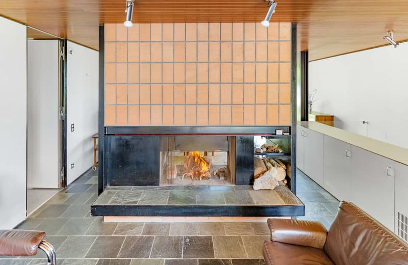 open fireplace with glass cover, stone hearth, brown leather armchairs, white walls, wooden ceiling