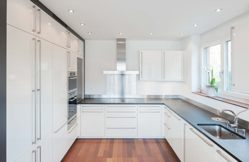 modern kitchen with white cabinets, black granite countertops, integrated appliances, wooden floor, stainless steel backsplash, ceiling lights, a window