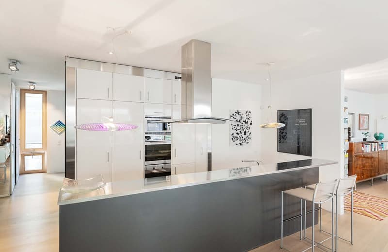 stainless steel kitchen, central island with bar stools, microwave, oven, range hood, hanging lamps, wooden floor, built-in cabinets