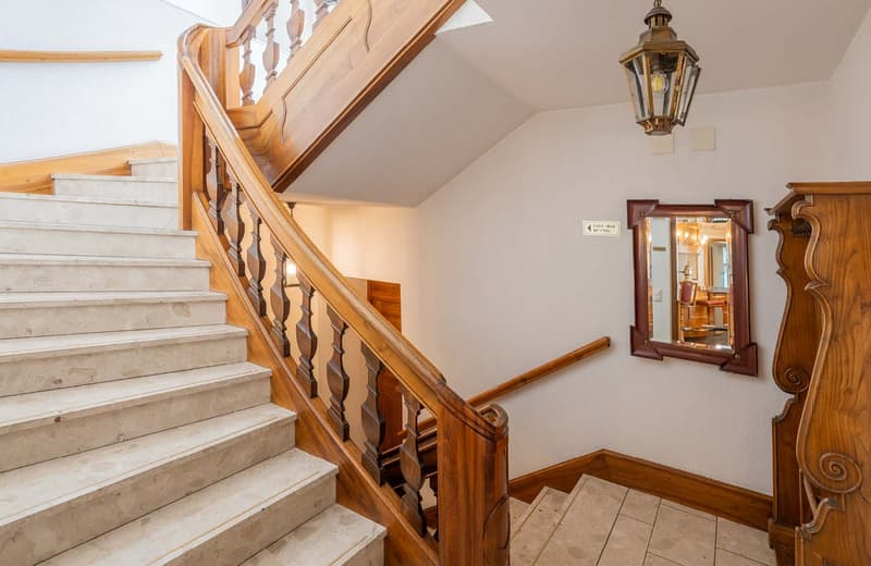 Wooden staircase with ornate railing, marble steps, antique-style light fixture, and a decorative mirror on the wall