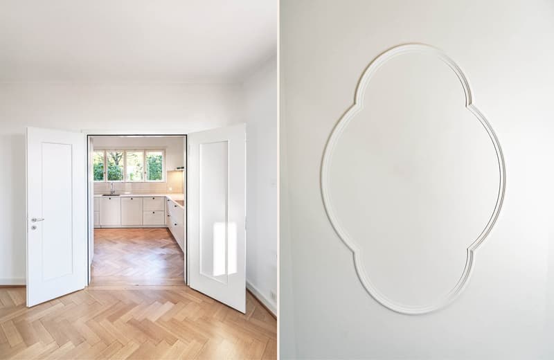 Open door leading to a kitchen with wooden floor and modern cabinets, wall-mounted power outlet, large windows, open doorway