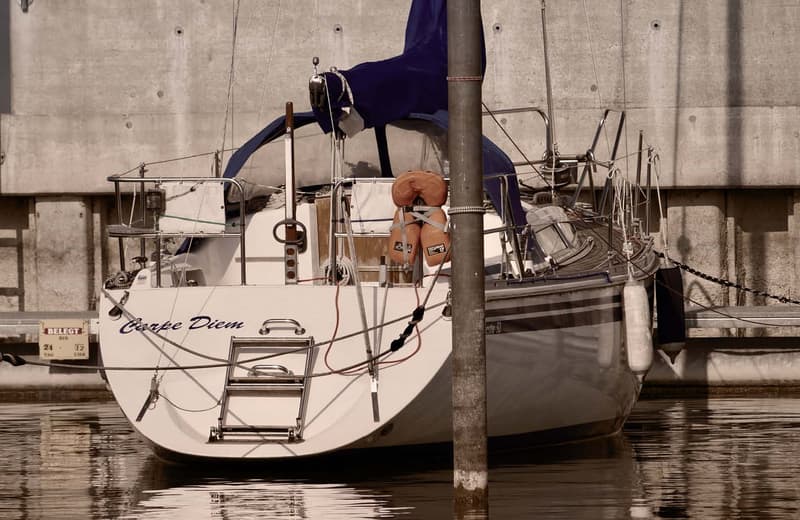 A sailboat named 'Carpe Diem' docked in a harbor, with various sailing equipment and rigging visible on the boat.