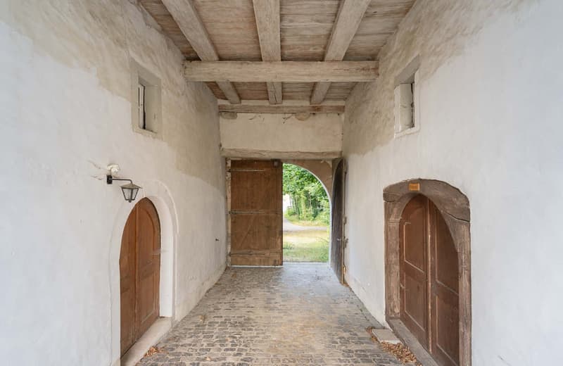 white walls, wooden beam ceiling, brick floor, arched doorways, open arch leading to green space