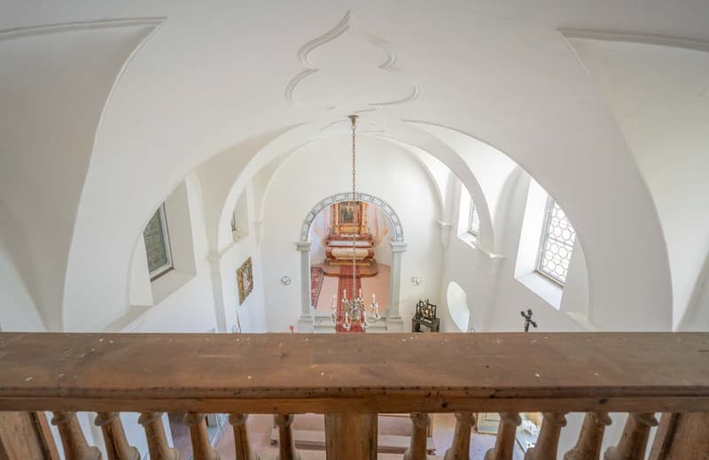 vaulted ceiling, chandelier, arch openings, wooden railing, framed picture, decorative elements, tiled floor, arch windows, red rug, furniture