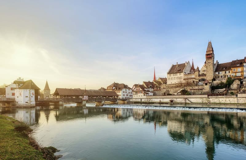Picturesque town with historic buildings, a river, and a covered bridge. The town has a medieval or old-world charm with its architecture and scenic setting.