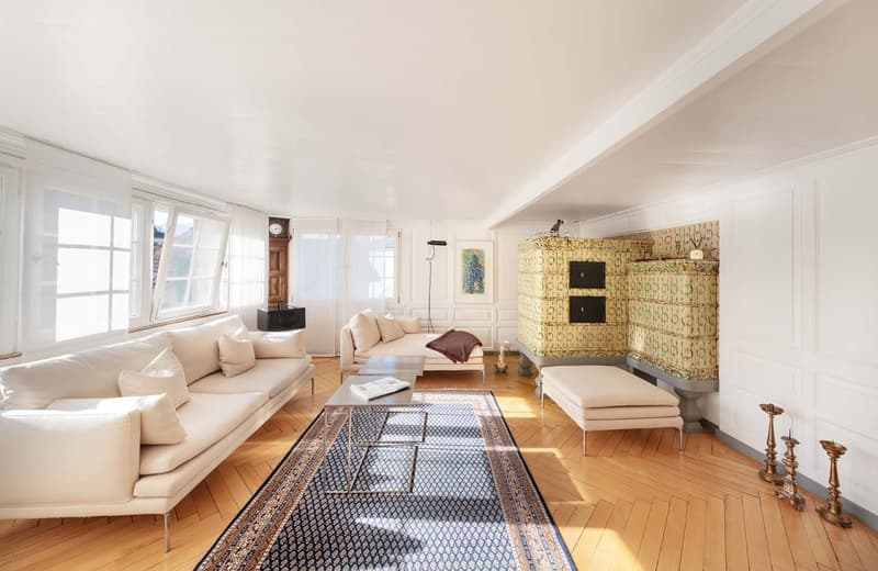Living room with white walls, wooden floor, large windows, two sofas, coffee table, fireplace, rug, decorative items