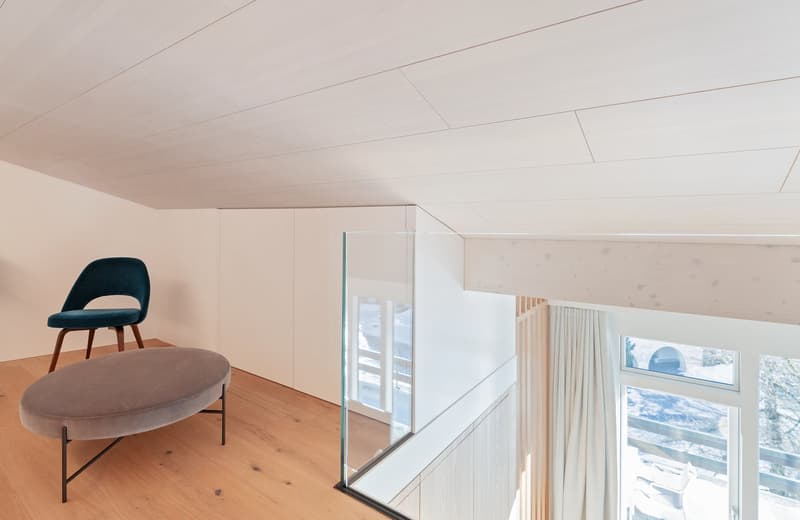 upstairs room with glass wall, brown floor, furniture includes a chair and ottoman
