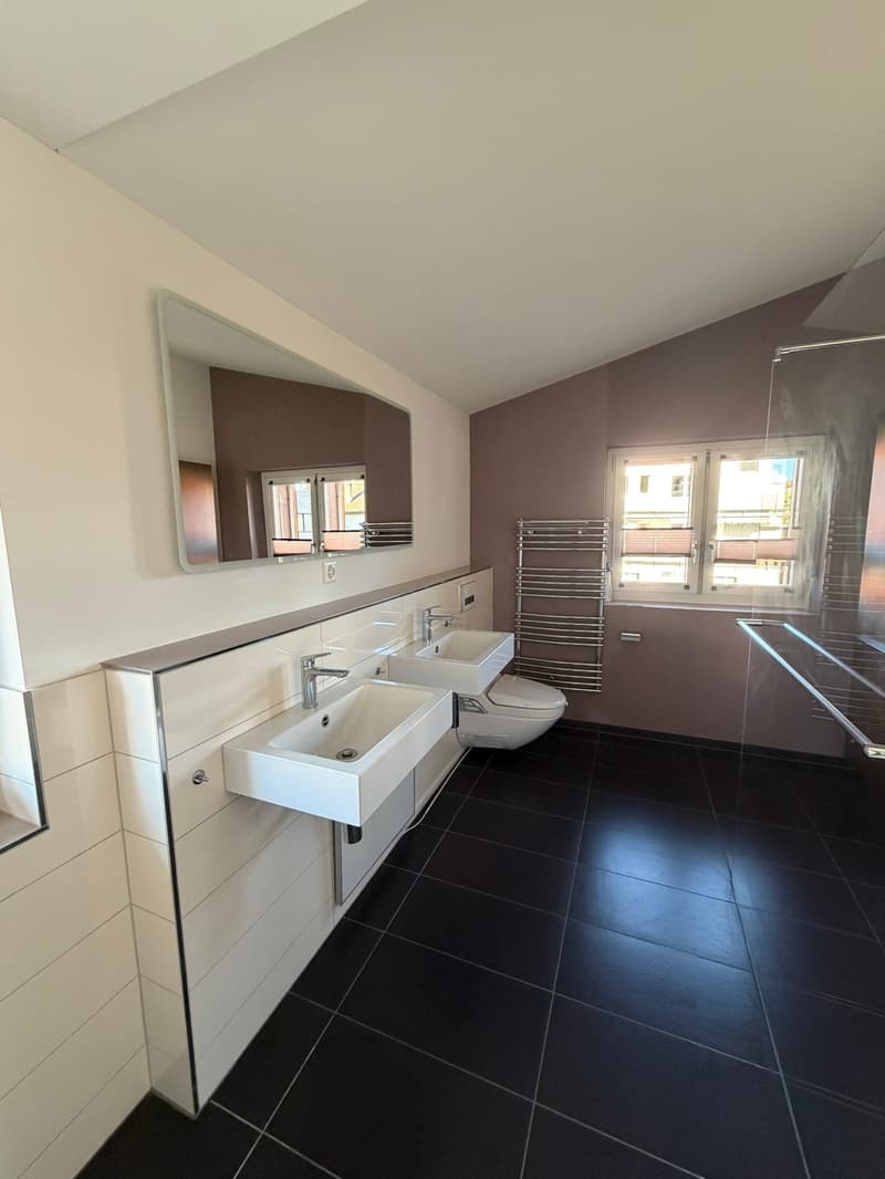 Bathroom with two sinks, toilet, mirror, glass shower enclosure, towel rack, and window.