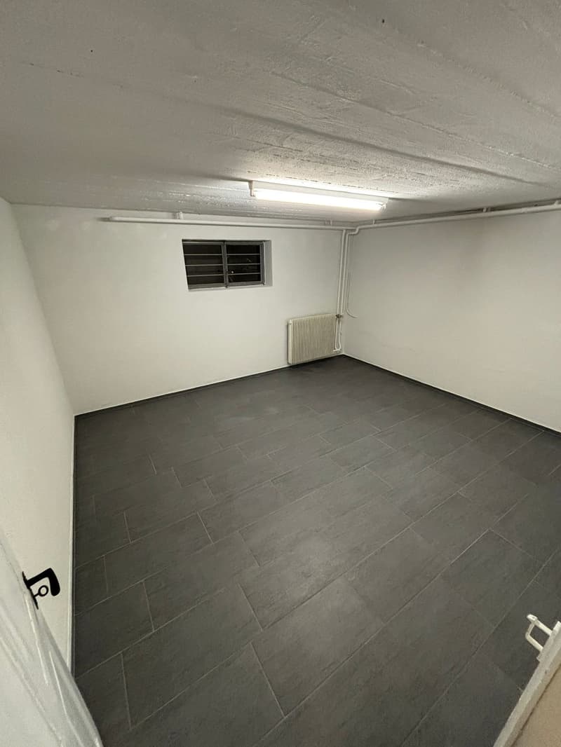 Empty room with white walls, gray tiled floor, small window, and a radiator