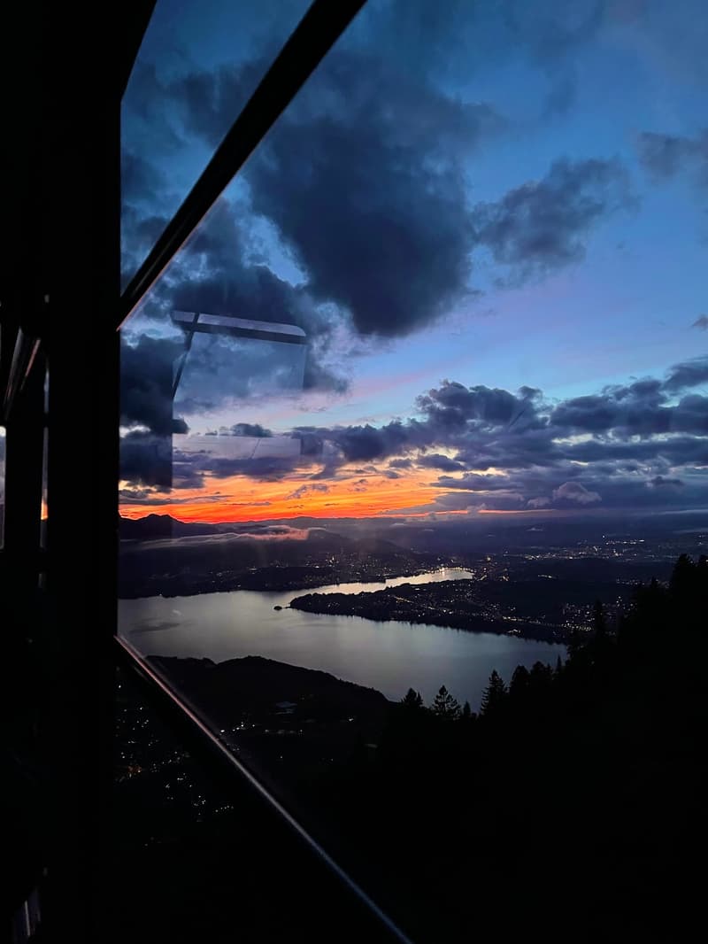 Sunset view from a high vantage point, showing a city skyline, a body of water, and a mountainous landscape.