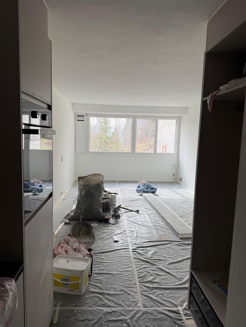 empty room, white walls, floor covered with plastic sheet, window, cabinets, tools and materials on the floor