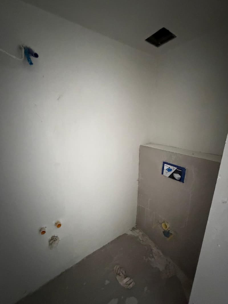 unfinished room, white walls, gray floor, electrical outlets, plumbing fixtures