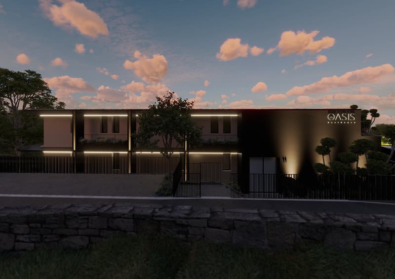 Modern building with a black facade, illuminated by lights, two floors, a tree in front, and a stone wall at the bottom.