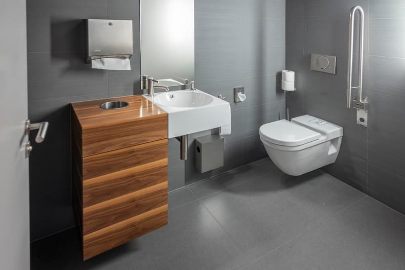Modern bathroom with gray tiles, wooden vanity, white sink, and silver fixtures