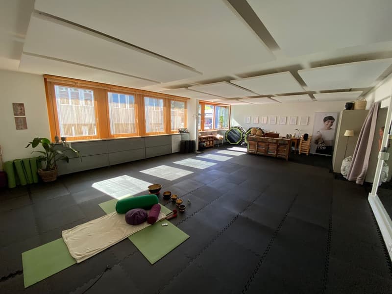 large room, black floor, yoga mats, yoga props, large windows, potted plant, wooden furniture, picture frames