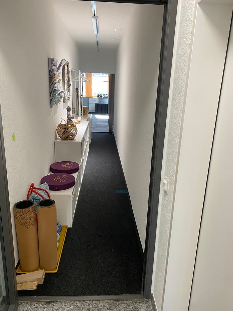 hallway with white walls, black carpet, white shelves, decorative cushions, wicker basket, storage boxes, yoga mats, open door