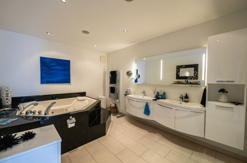 two sinks, bathtub, large mirror, wall mounted towel rack, floor lamp, shelf, towel basket, white tiles