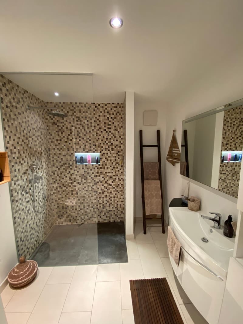 modern tiled bathroom with walk-in shower, vanity with sink, mirror, wooden floor mat, and towel rack