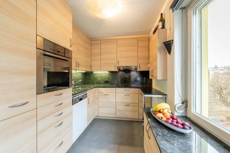 Modern fitted kitchen with wooden cabinets, granite countertops, integrated appliances, under cabinet lighting and a large window.