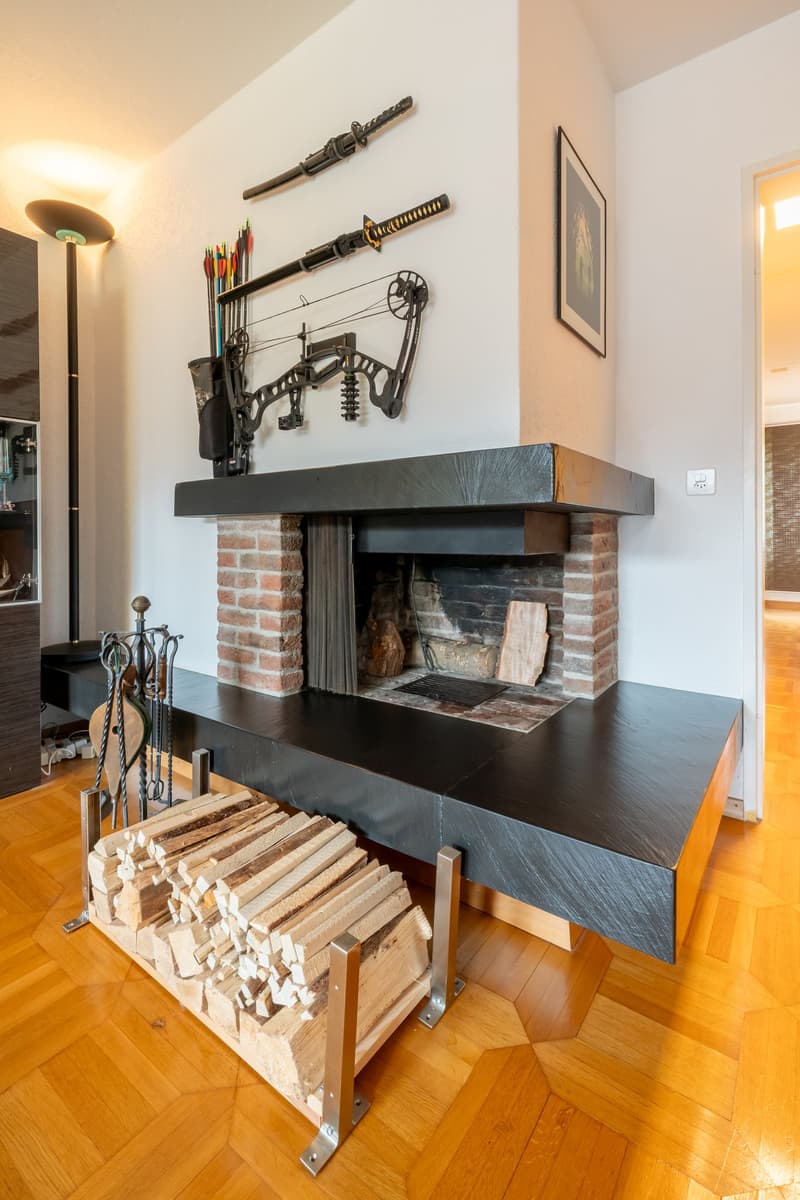 Wooden floor, fireplace, white walls, swords, bows and arrows on wall, frame on wall, light from lamp