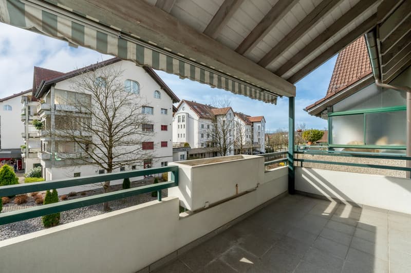 Balcony with green railings, tiled floor, white walls, awning, planter box, view of surrounding buildings