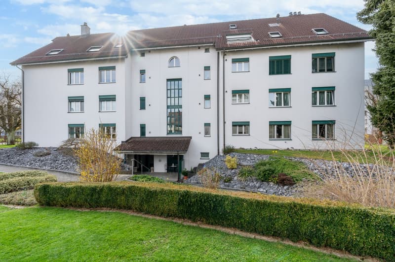 3 story white building, brown roof, green shutters, raised ground floor, garden, gravel path