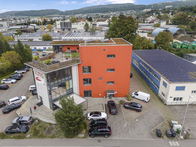 Industrial building with parking space in front, solar panels on the roof, orange facade, large glass windows