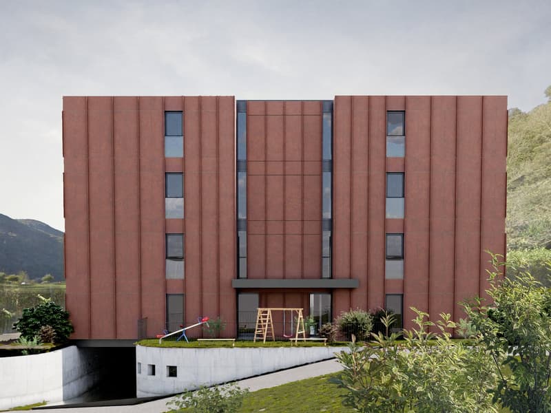 A modern multi-story building with a distinctive red brick facade, large windows, and a balcony or terrace visible on the upper floors. The building is surrounded by greenery and appears to be in a scenic, mountainous location.