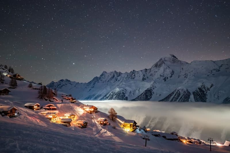 scenic winter mountain village landscape with snow-covered houses and mountains under starry night sky