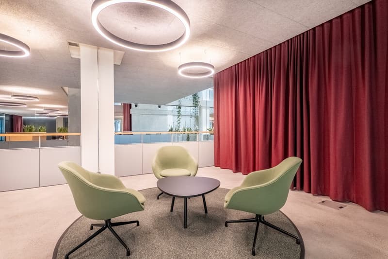 Contemporary meeting room with circular lights, a round table, and three green chairs on a round rug