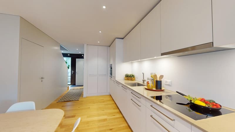 modern kitchen with white cabinets, wooden floor, induction stove, sink, dishwasher, washing machine, countertop, kitchen utensils, vegetables