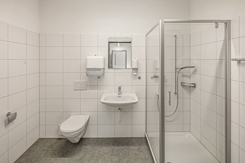 white tiled walls, white toilet, white sink, glass shower enclosure, mirror, soap dispensers