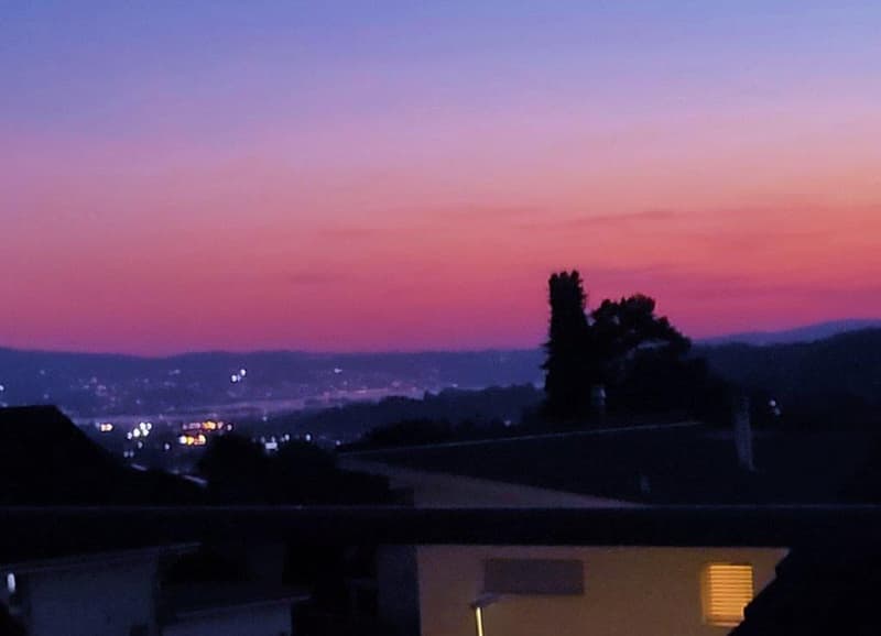 Sunset view from a balcony, cityscape, mountains, trees, and a clear sky