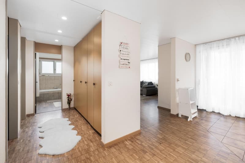 a hallway with wooden floor, a large white rug, a white cabinet, white walls, and large windows with white curtains