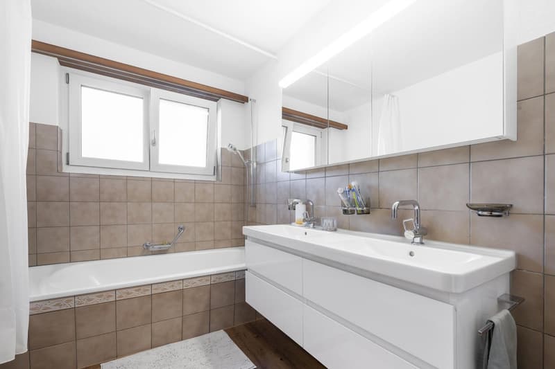 White bathtub, large mirror, two sinks, white tiles, white fixtures