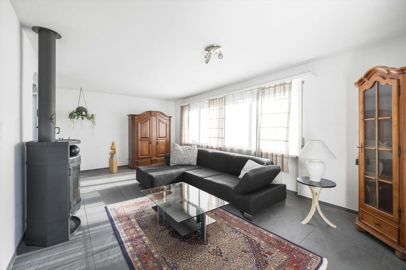 gray sectional sofa, glass coffee table, side table, lamp, fireplace, rug, wooden cabinets, windows with curtains, wooden wall art