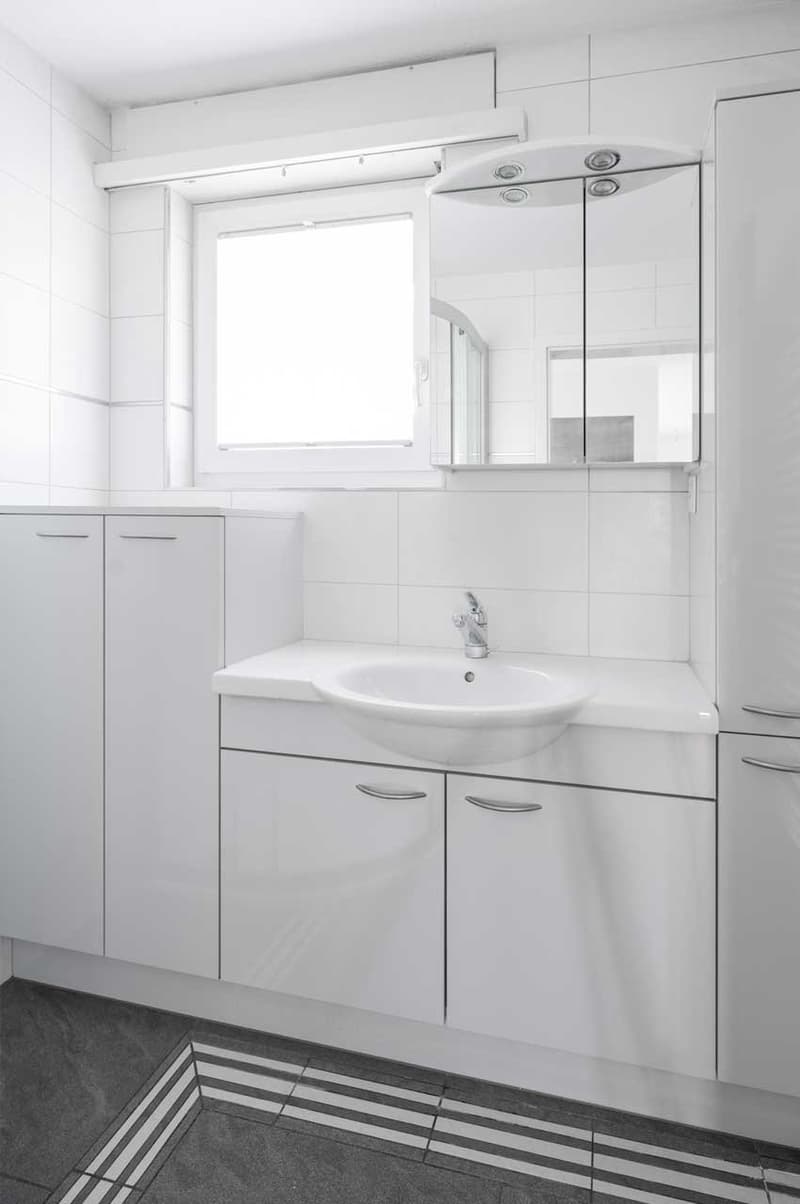 Modern bathroom with white cabinets, sink, mirror, and tiled flooring