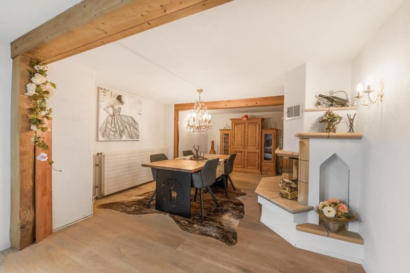 wooden floors, white walls, chandelier, dining table with chairs, wooden cabinet, fireplace with decorative items, radiator, floral decorations