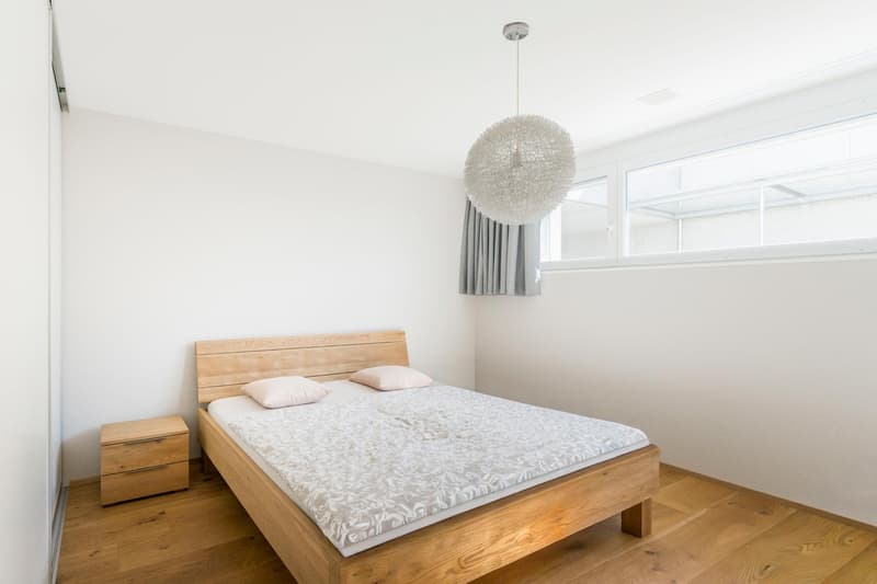 modern bedroom with wooden bed, white walls, wooden floor, large window, pendant light, nightstand