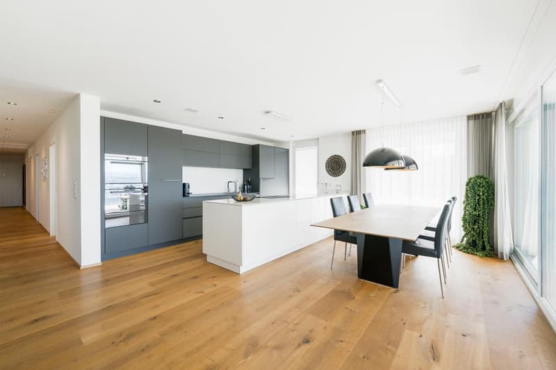 modern kitchen with white island, gray cabinets, wooden floor, large windows, dining table, black chairs