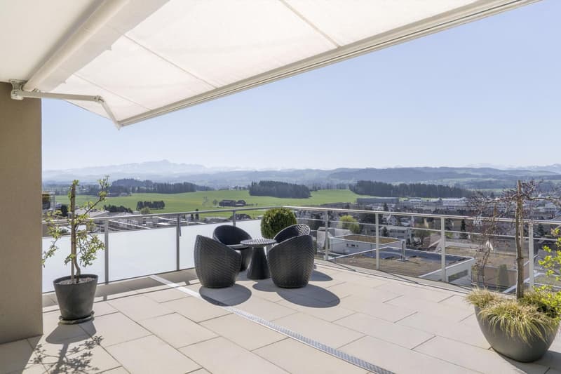 Balcony with a view of the mountains, two wicker chairs, a small table, and two potted plants.