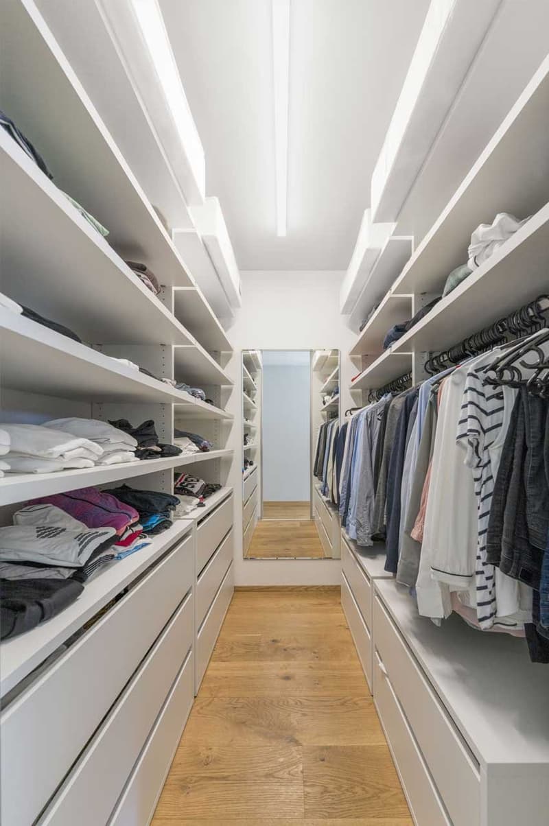 walk-in closet with white shelves, wooden floor, clothes hanging on racks, mirror