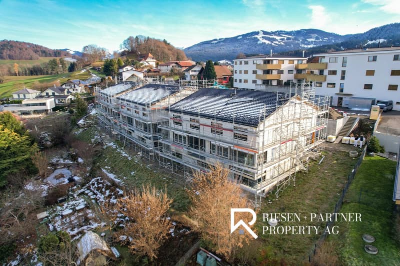 Construction site of an apartment building with multiple floors, surrounded by trees and mountains in the background.