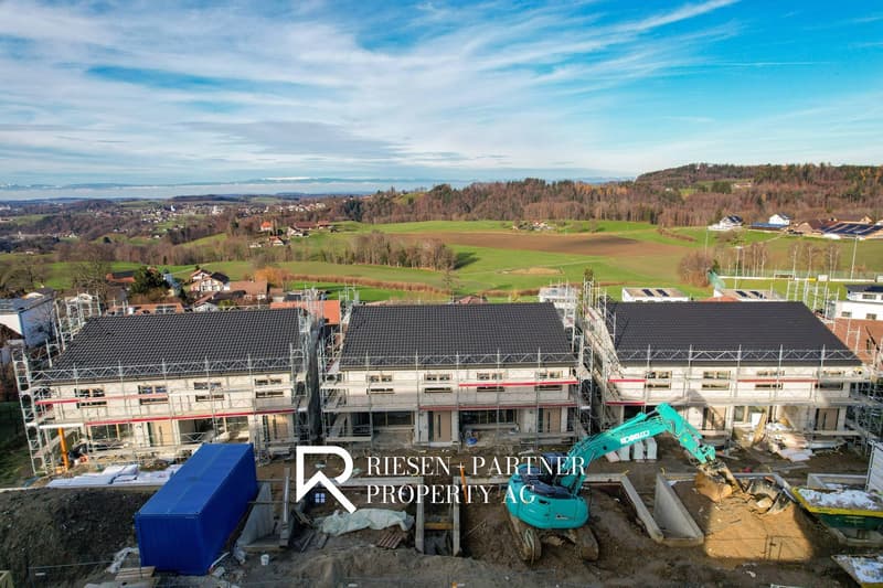 New apartment buildings under construction, each with modern architectural design, surrounded by a rural landscape with green fields and distant hills.