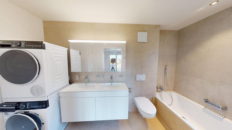 Bathroom with white bathtub, toilet, double sink, and two white washing machines.