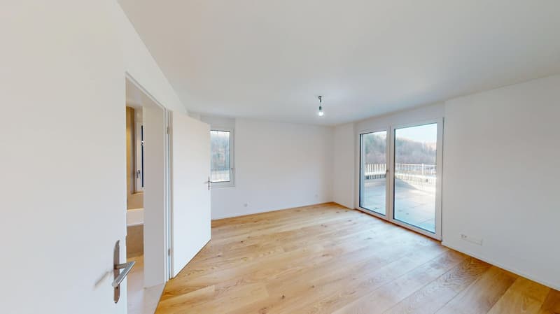Open room with white walls, hardwood floor, sliding glass doors leading to balcony