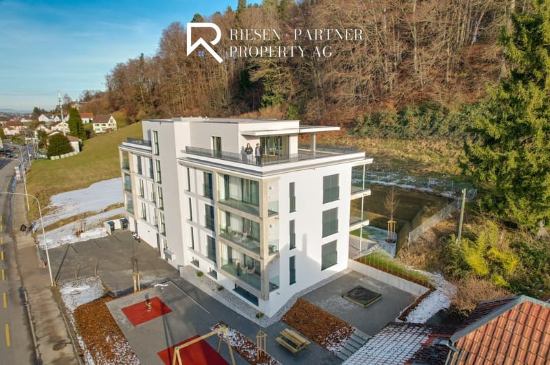 modern multi-story building, raised ground floor, balcony, parking spaces, red carpet outside, green grass, trees, sidewalk